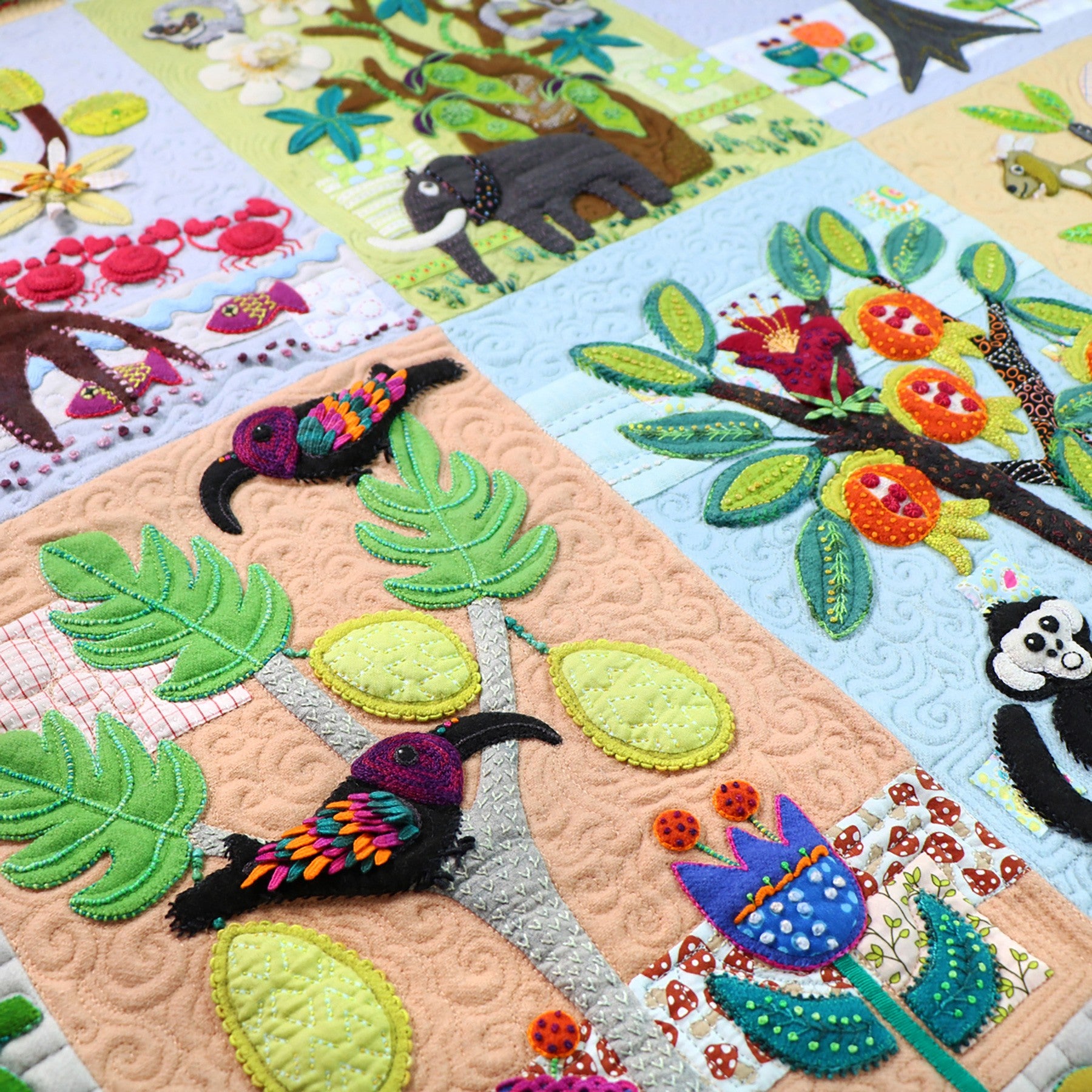 Close-up of a Forest for the Trees block, a tropical tree with broad leaves, a toucan, and a panda appliqued in wool with textural embroidery.