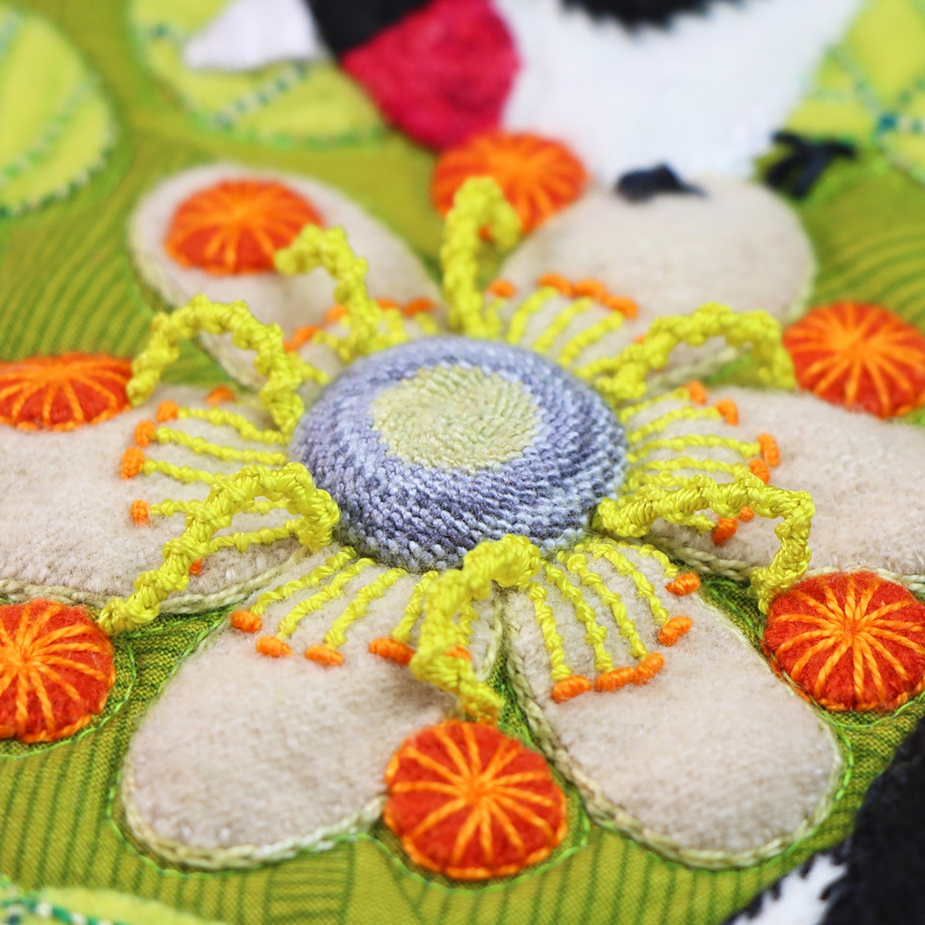 Close-up of dimensional embroidery on a Forest for the Trees block, a flower worked in raised stitches and bullion knots in orange, yellow, and purple.