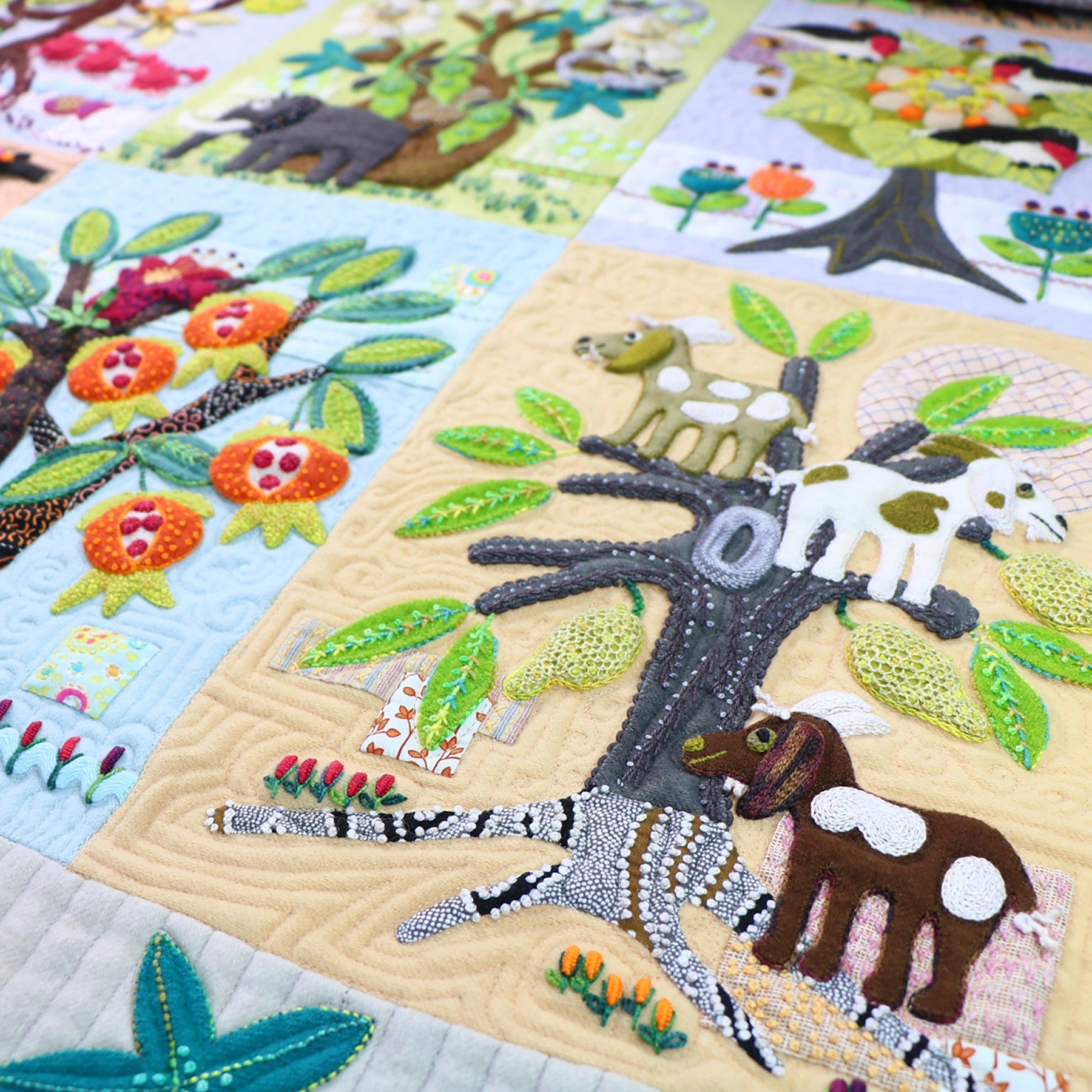 An angled view of the Forest for the Trees quilt, showing a tree block with a giraffe and other animals worked in layered wool with hand embroidery over a quilted background.