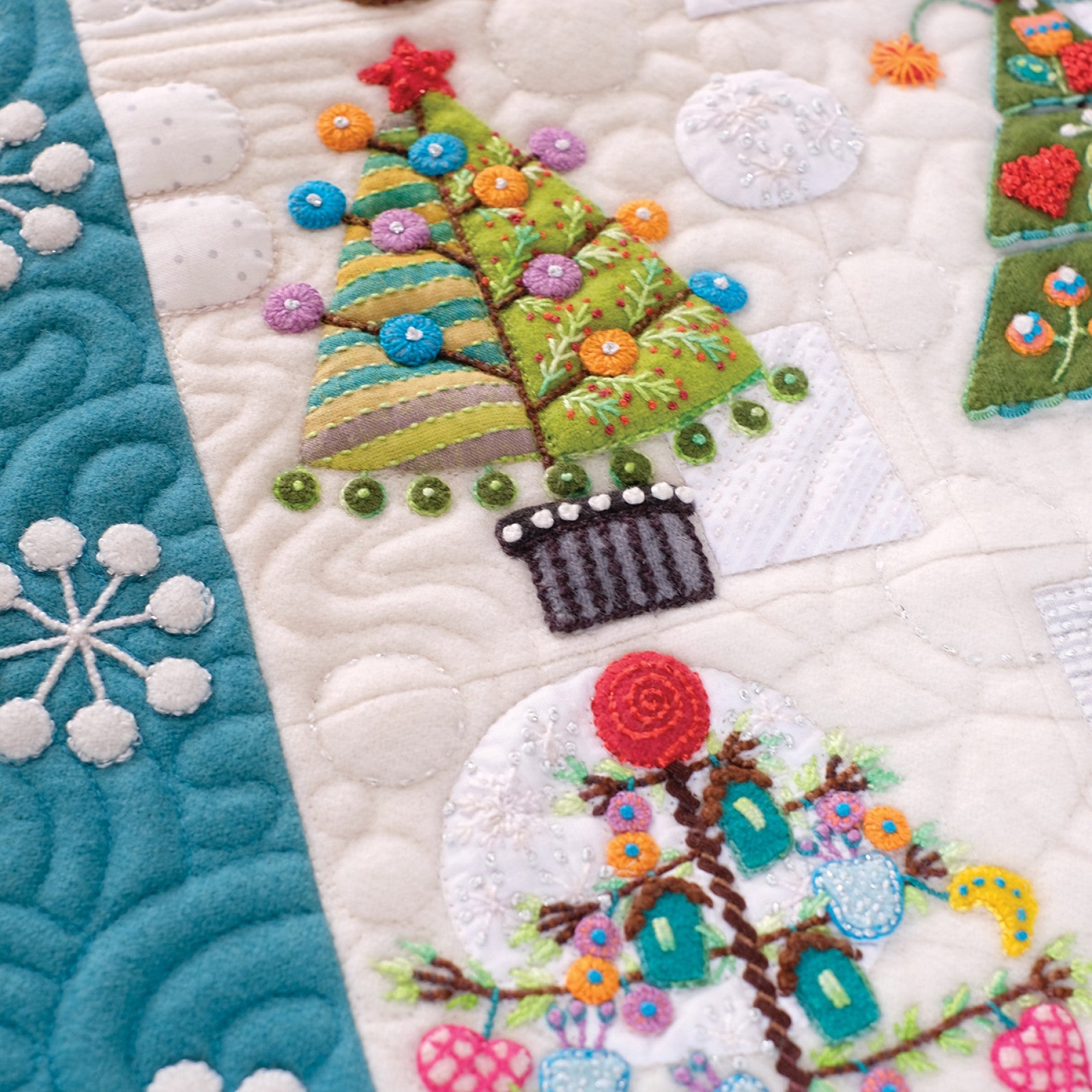 Close detail of Tinsel blocks by Sue Spargo of Folk Art Quilts. Decorated wool Christmas trees with beaded ornaments and a green garland, in layered applique and dense hand embroidery on a quilted white background.