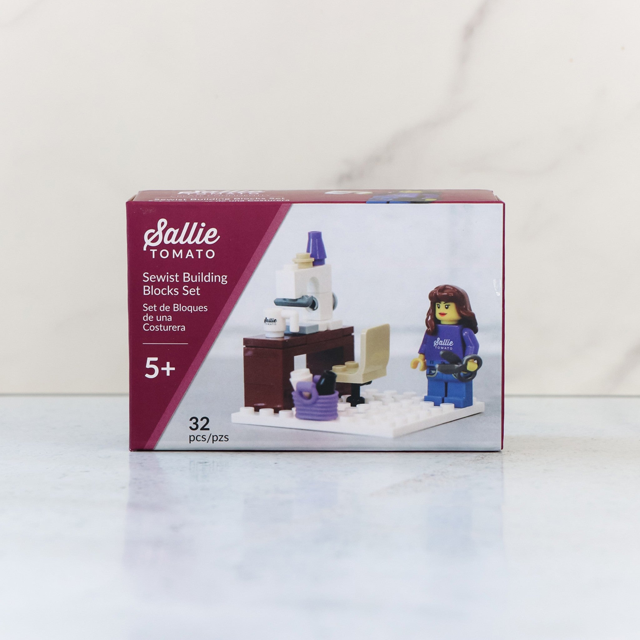 Sallie Tomato Sewist Building Block Set box showing the finished build and a sewist figurine in a purple Sallie Tomato shirt holding oversized scissors. Labeled as a 32-piece set.