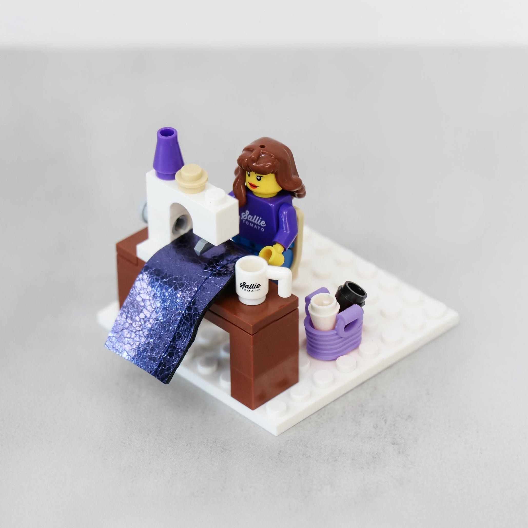 Sallie Tomato Sewist Building Block Set shown from the front: sewing machine, work table, swivel chair, accessories, and a sewist figurine on a white base.