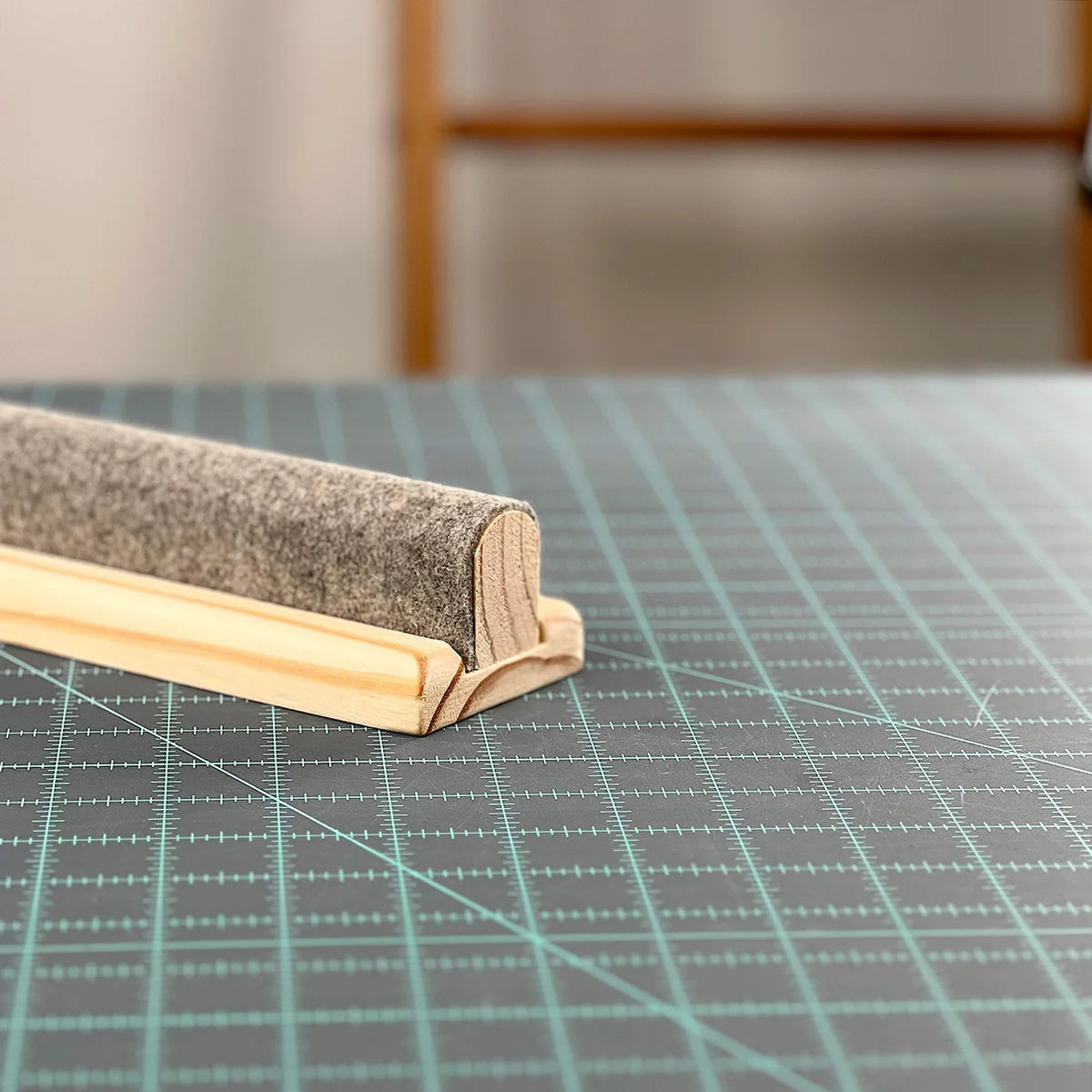 Close-up end view of The Gypsy Quilter Wool Pressing Bar on a green cutting mat, the gray wool rounded top seated in the routed channel of the molded light wood clapper base.