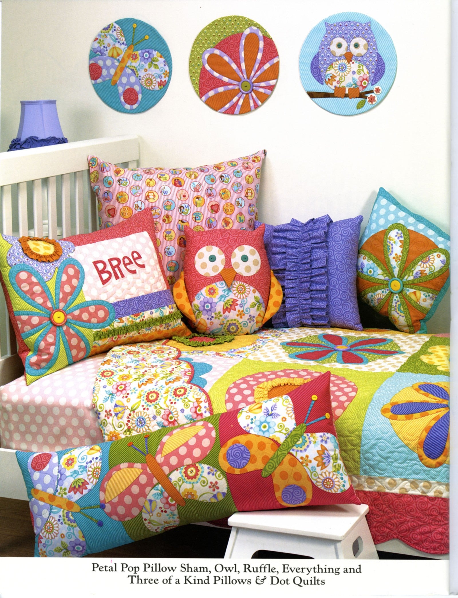 Interior page of the Curiosities and Mischief quilt pattern book by Nancy Halvorsen of Art to Heart, showing a child's bed with the Petal Pop pillow sham, owl pillow, ruffle pillow, and dot quilts.