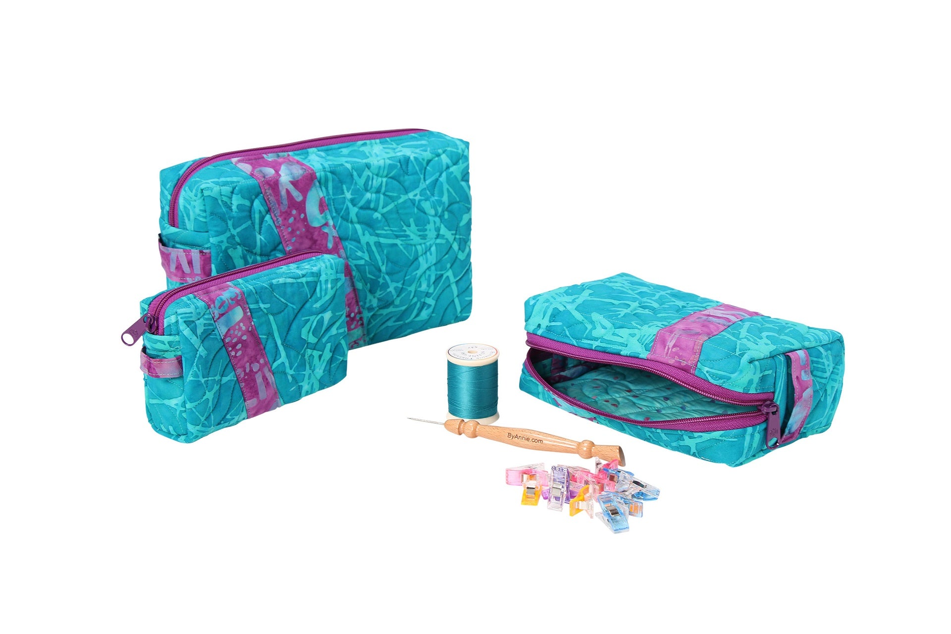 Two Ditty Bags in teal prints with one unzipped and open beside a spool of thread and sewing tools, showing the side handles and zippered top.