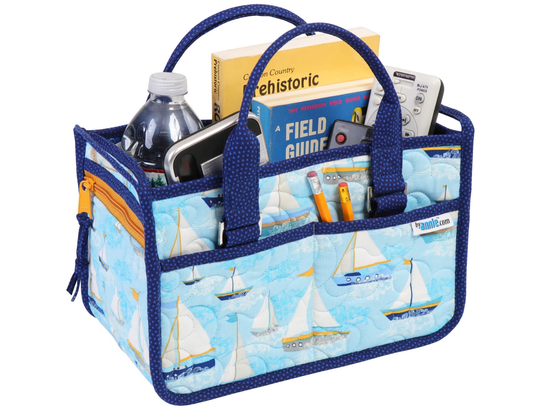 In Control Caddy sewn in a blue sailboat print, filled with a field guide, a water bottle, and tools in the exterior slip pockets, with padded fabric handles standing upright.
