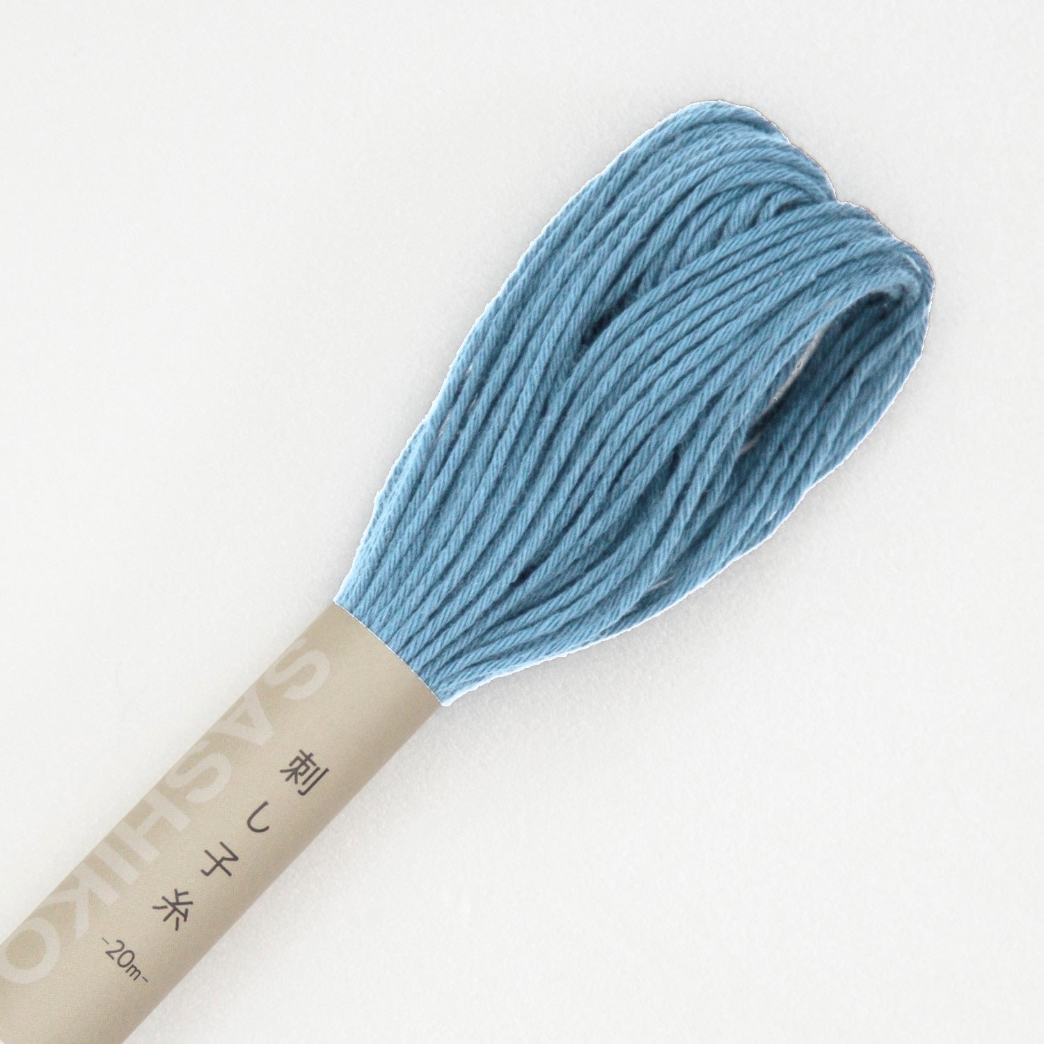 Olympus sashiko thread in sky blue, a close view of the looped end of a dusty sky-blue cotton skein above its kraft SASHIKO paper band, on a white background.