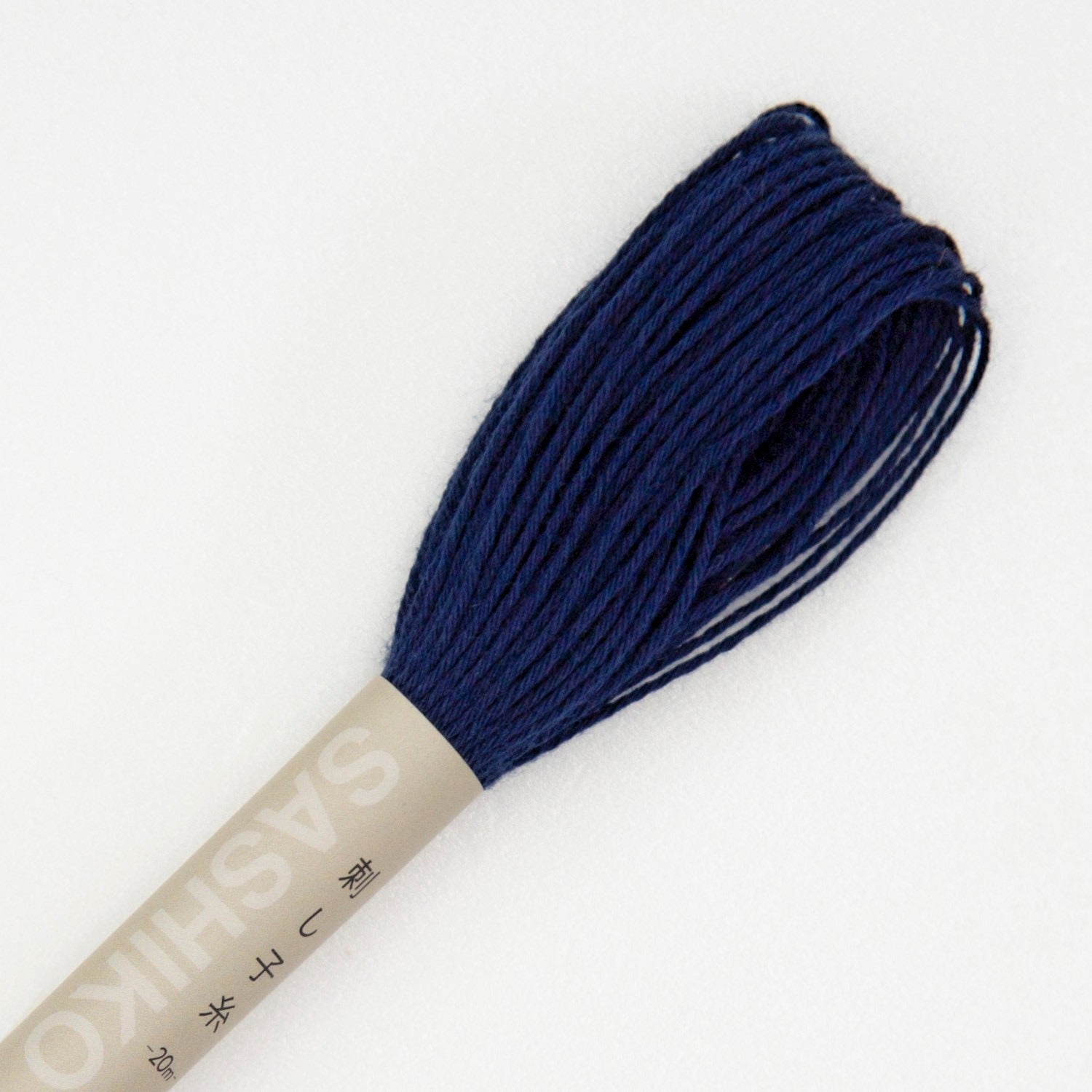 Olympus sashiko thread in navy, a close view of the looped end of a deep navy-blue cotton skein above its kraft SASHIKO paper band, on a white background.