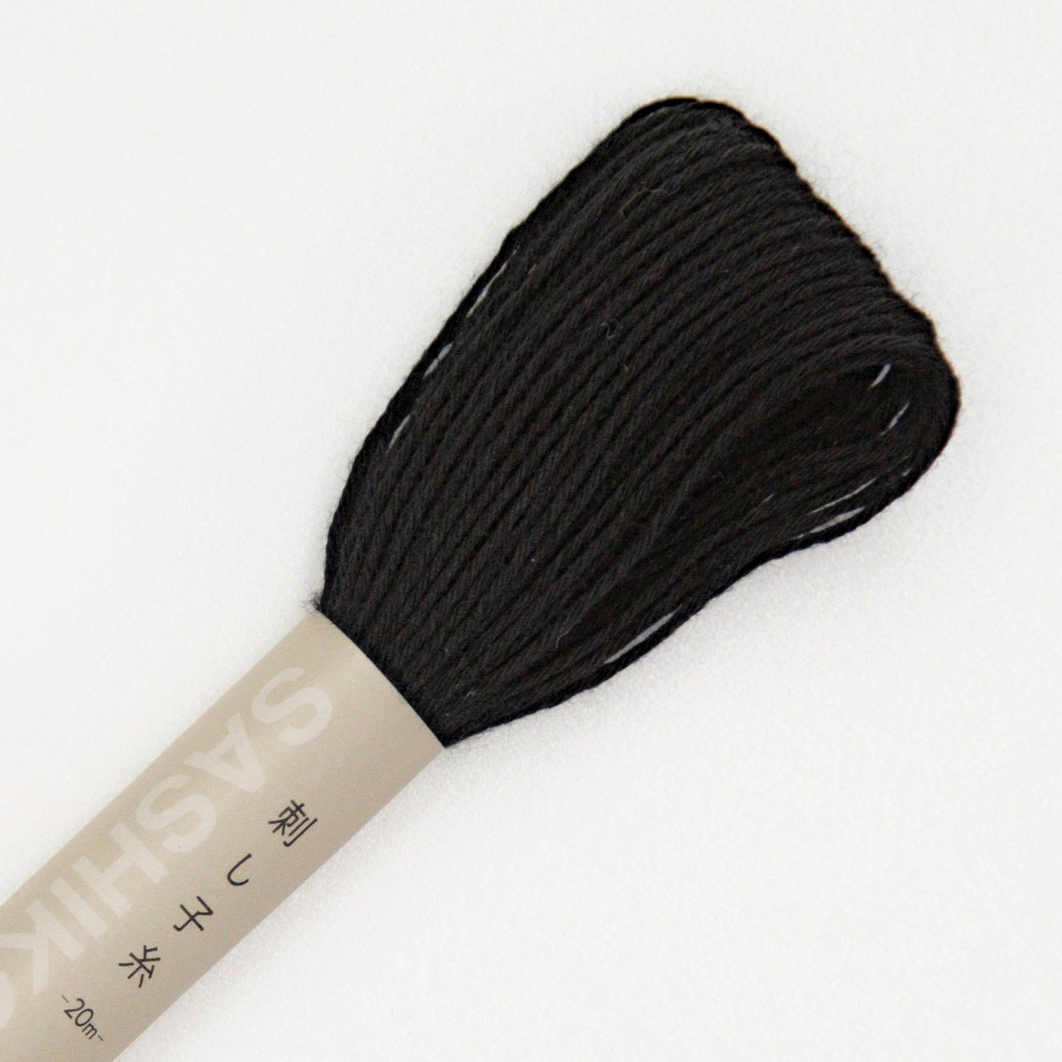 Olympus sashiko thread in black, a close view of the looped end of a black cotton skein above its kraft SASHIKO paper band, on a white background.