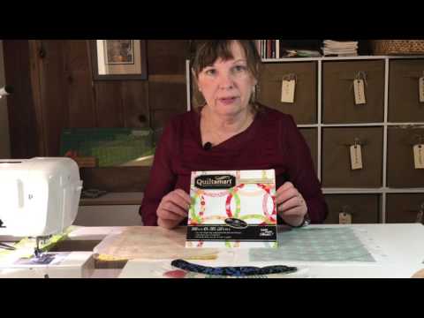 Video demonstrating the Quiltsmart Double Wedding Ring method: sewing a 2.5-inch fabric strip on the printed interfacing line, trimming and turning it, fusing it to the background, and zigzag stitching the arc.