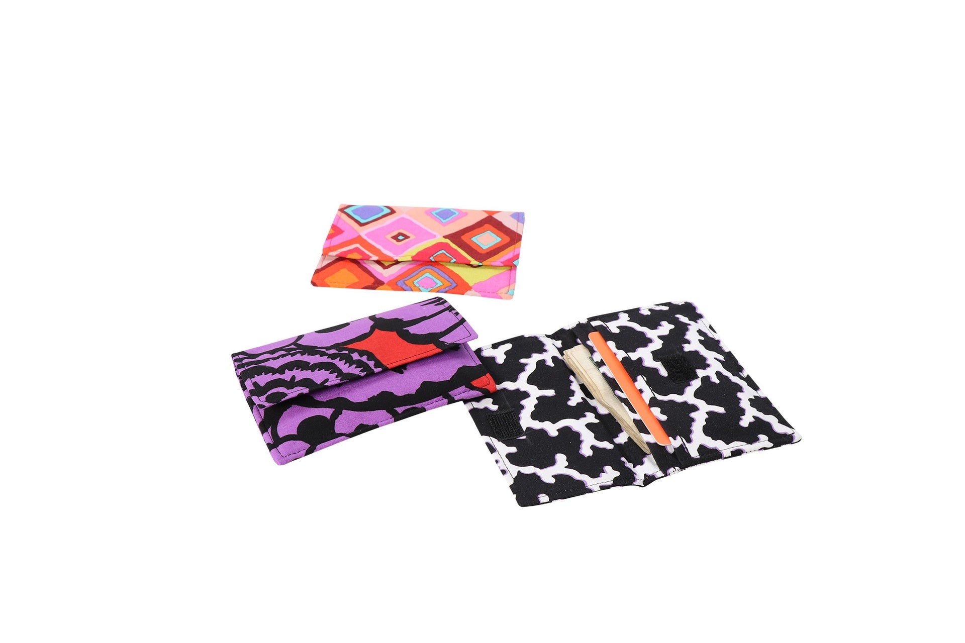 Three Sew Simple Wallets in purple and pink prints shown closed with their flaps folded over.