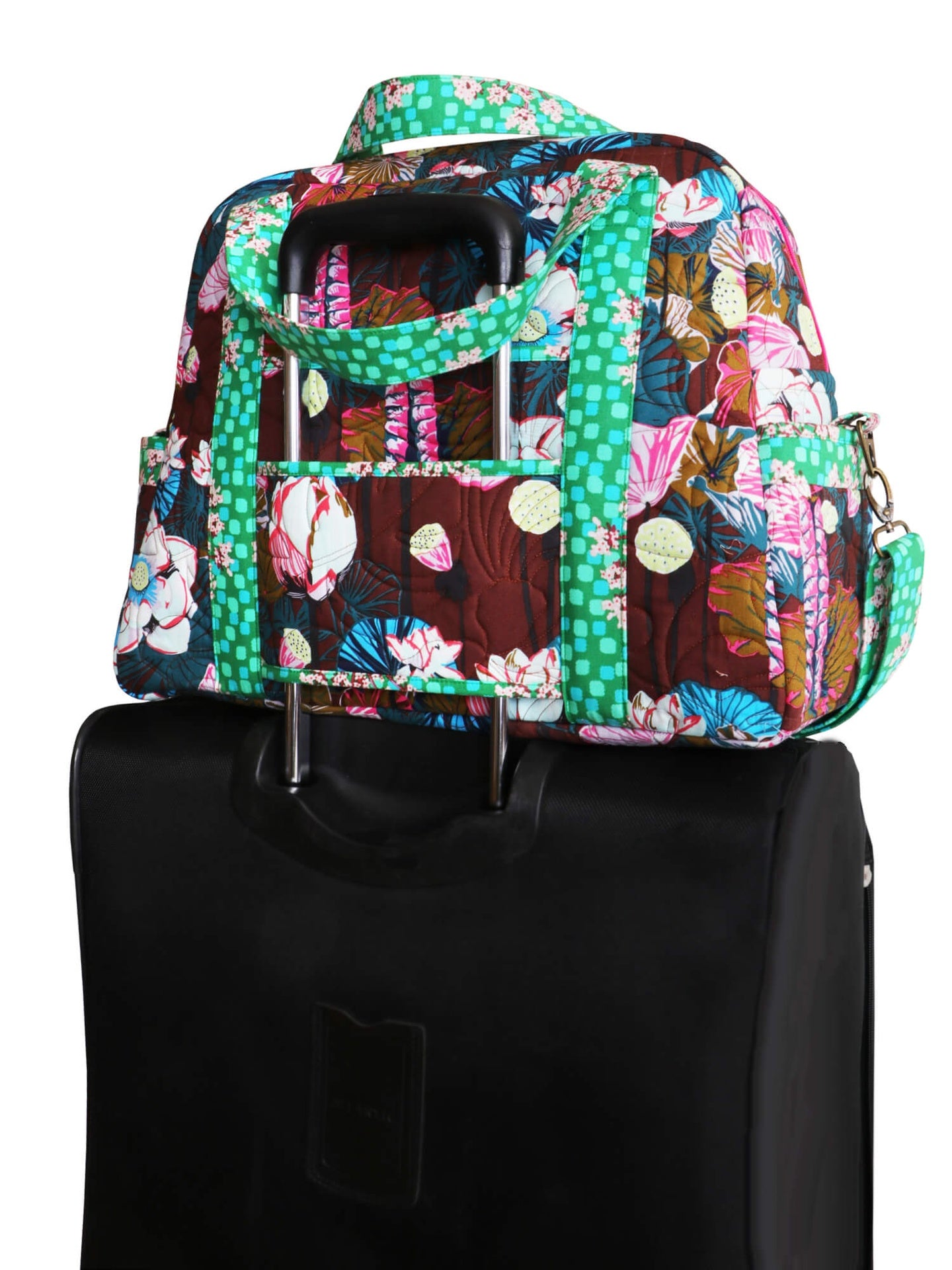 An Ultimate Travel Bag in a green print sitting on a rolling suitcase, with the trolley sleeve slipped over the luggage handle.